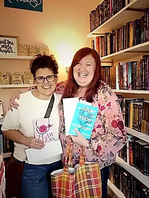 Two women laughing together in a bookstore, each holding a book — a candid friendship photo used for a custom acrylic photo magnet from Grey Barn Handwerk