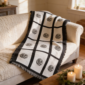 Nine panel sublimation blanket with black grid border and botanical medallion print draped over a cream sofa in a warm farmhouse living room with candles and greenery