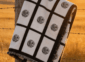 Nine panel sublimation blanket with black grid border and botanical medallion print folded over a weathered wooden fence post in a golden Saskatchewan prairie field at sunset