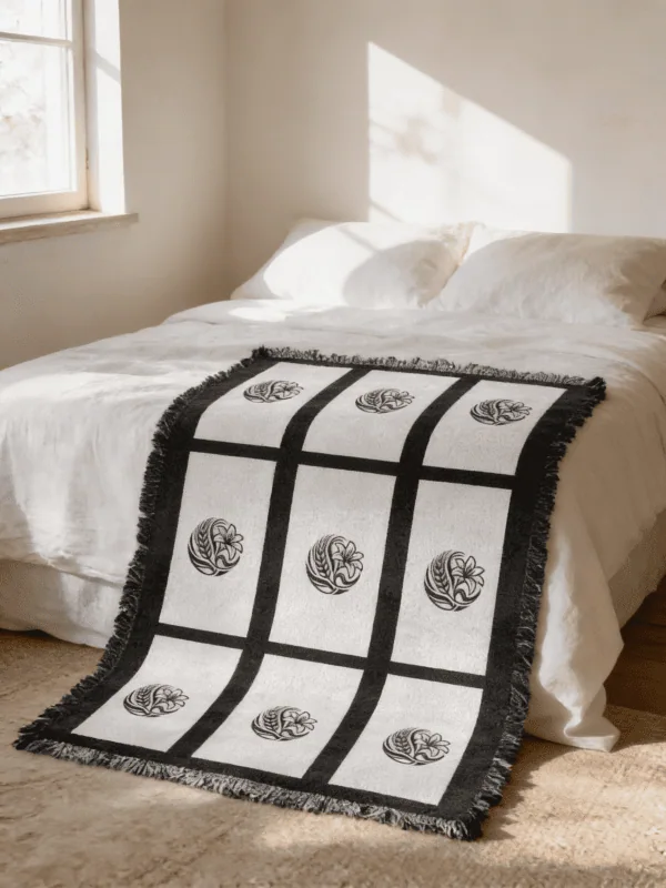 Nine panel sublimation blanket with black grid border and botanical medallion print layered at the foot of a bed with white linen bedding in a neutral boho bedroom