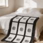 Nine panel sublimation blanket with black grid border and botanical medallion print layered at the foot of a bed with white linen bedding in a neutral boho bedroom