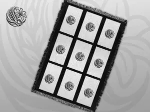 Black and white woven throw blanket with fringed edges featuring a nine-panel grid design, each panel centred with a circular prairie botanical logo of wheat and wildflowers