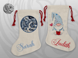 Winter Village & Gnome Personalised Linen Christmas Stocking | Grey Barn Handwerk Saskatchewan Two natural linen Christmas stockings with red drawstring ties — one with a blue circular winter village scene personalised with the name Sarah, the other with a whimsical Christmas gnome personalised with the name Judith in red script