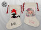 Two natural linen Christmas stockings with red drawstring ties — one with a grumpy black cat in a Santa hat personalised with the name Ash, the other with a soft illustrated angel girl with roses personalised with the name Ellie in pink script