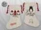 wo natural linen Christmas stockings with red drawstring ties — one featuring three red plaid Christmas gnomes with the text "Gnome for the Holidays" and the name Stevie in red script, the other with a music-loving penguin and hand-lettered "Let's Sing Christmas Songs" with the name Smitty in black script